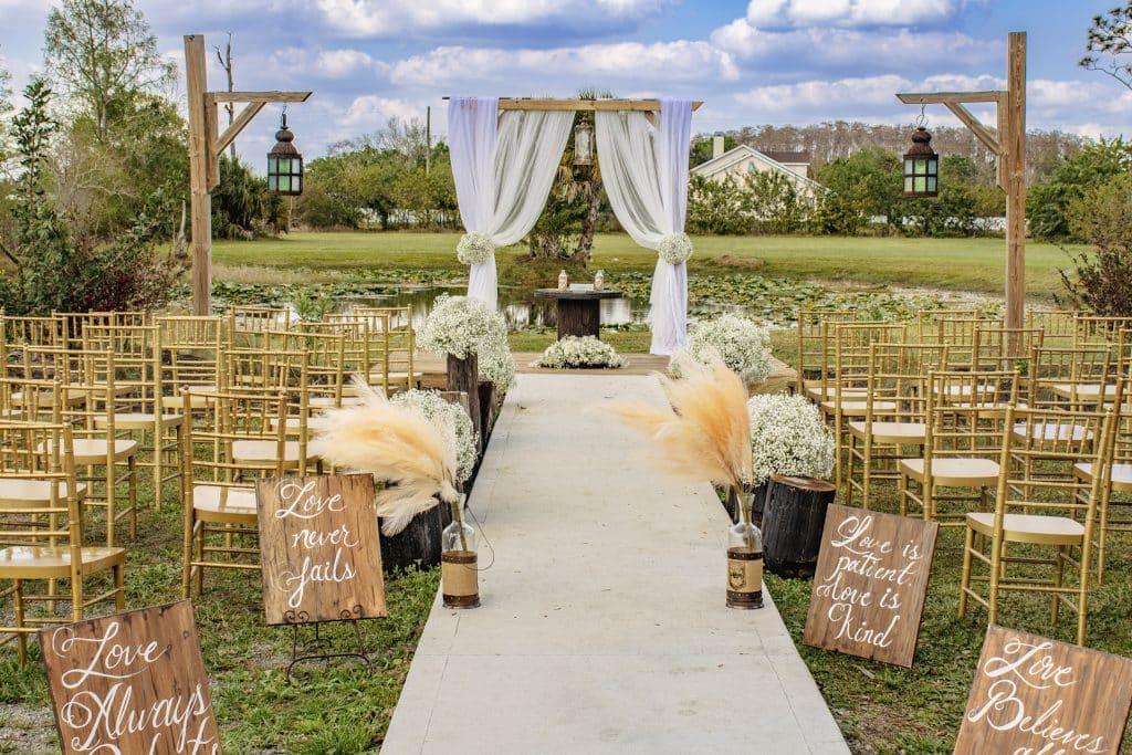 outdoor wedding ceremony with aisle signs. lanterns and wooden posts draped in white planned by Soulovevent LLC