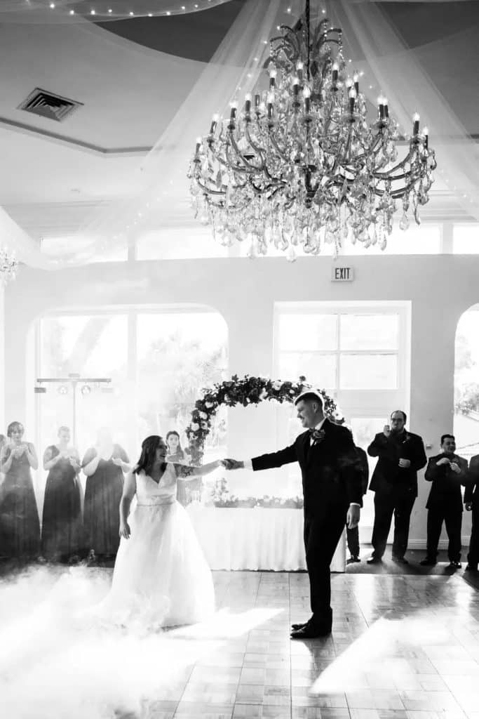 black and white photo of bride and groom dancing on a cloud under large chandelier at La Cita Country Club