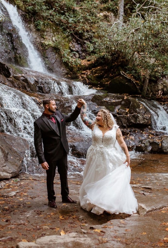 bride and groom dancing at the base of a waterfall wearing wedding gown and suit from Carolyn Allen’s Bridals & Formals