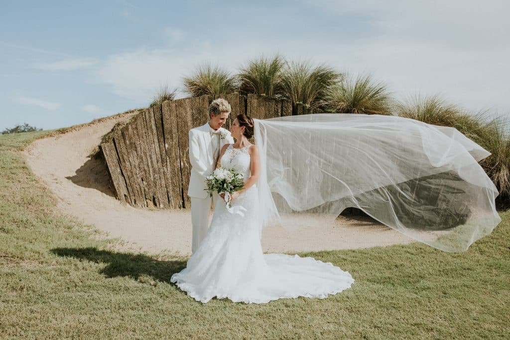 couple wearing wedding apparel from Carolyn Allen’s Bridals & Formals standing by a dune at the beach