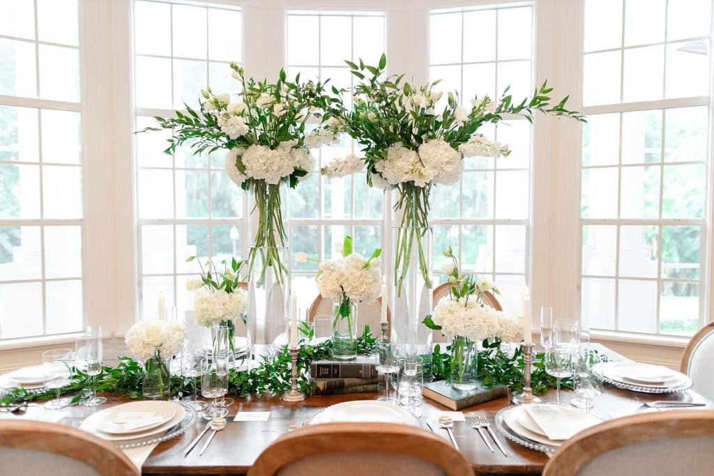 tall white centerpieces on table set against tall, paned windows coordinated by Julie Miner Events