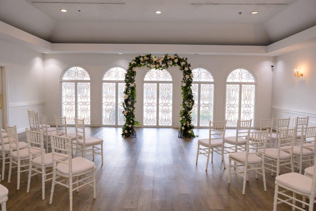 indoor wedding ceremony with green arch against arched windows at La Cita Country Club
