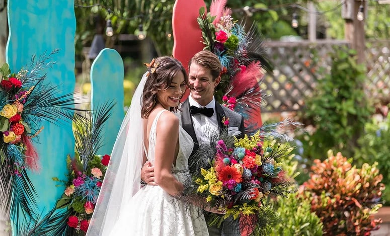 bride with tropical bouquet and groom with colorful pink and turquoise backdrop coordinated by Julie Miner Events