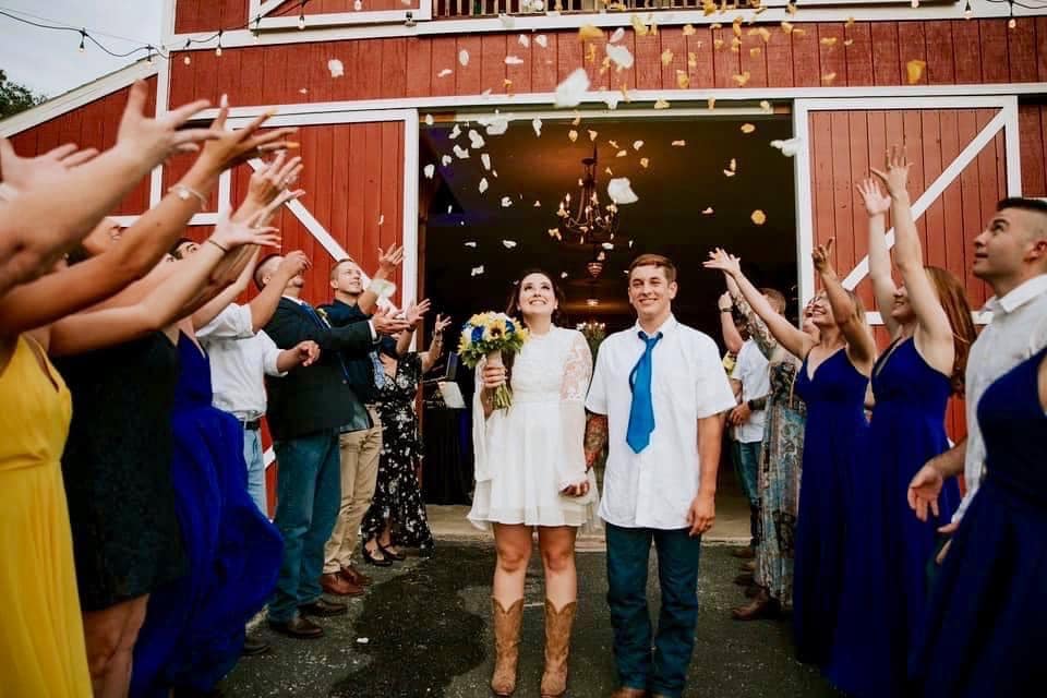bride on cowgirl boots and groom leaving wedding ceremony under shower of confetti at The Red Barn at Bushnell