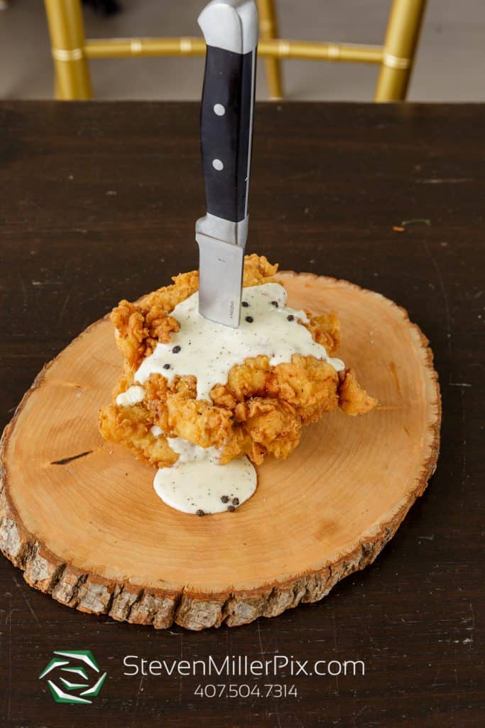 fried chicken breast with gravy and a large knife skewering it by Dubsdread Catering