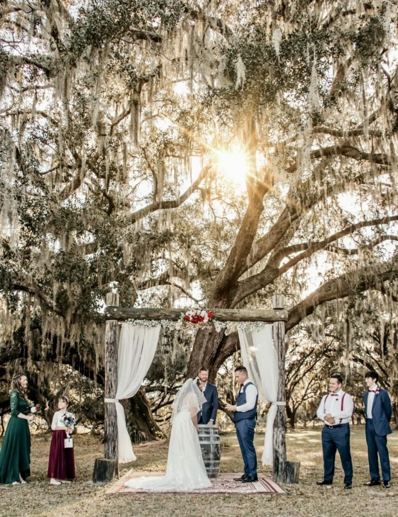 bride and groom under wooden altar outside under oaks draped in Spanish moss as the sun sets at The Red Barn at Bushnell