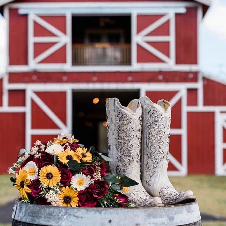 brides cowgirl boots and black eyed Susan and daisy bouquet in front of hay barn at The Red Barn at Bushnell