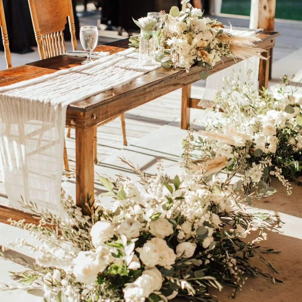 wooden sweetheart table with lace runner and large white bouquets and white and green floral centerpieces by Ian Tafoya Designs