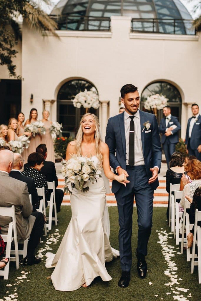 bride with beautiful and lush pink and white bouquet of roses by Ian Tafoya Designs laughing as she walks down the aisle with her groom