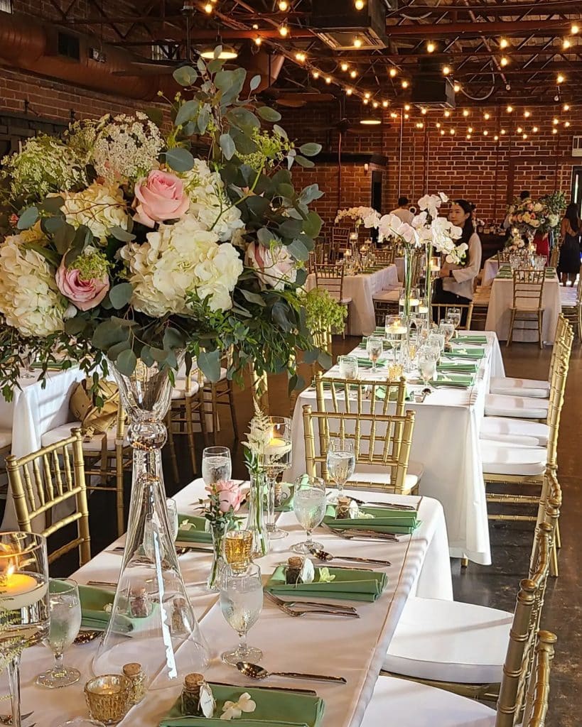 wedding reception with tall centerpieces of pink roses and white hydrangeas by Ian Tafoya Designs, long trestle tables and Chiavari chairs under market lights