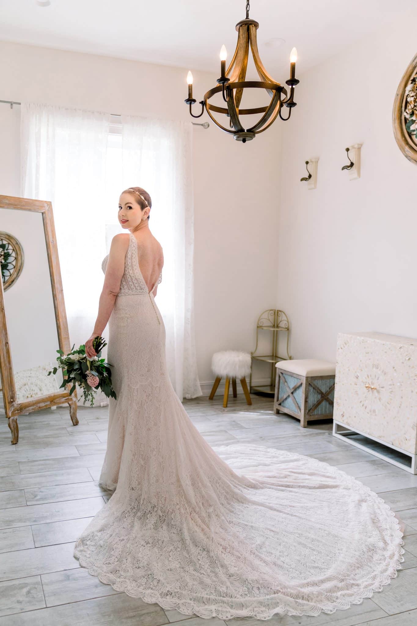 Bride, Amanda, stands in front of mirror at Bending Branch Ranch moments before her wedding vow renewal in her sleeveless, open back, wedding dress by The Bridal Finery.