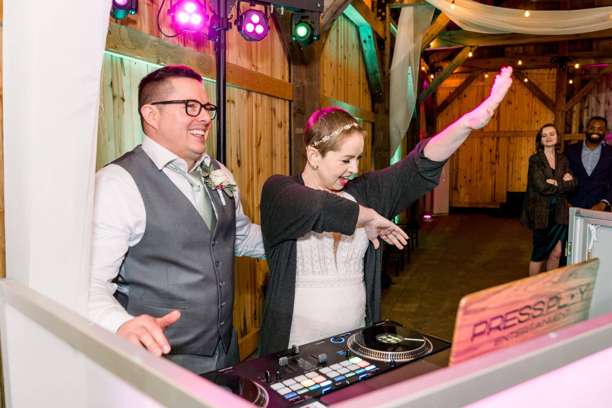 Bride and groom stand behind the DJ booth laughing and jamming out to music at their wedding vow renewal reception at Bending Branch Ranch.