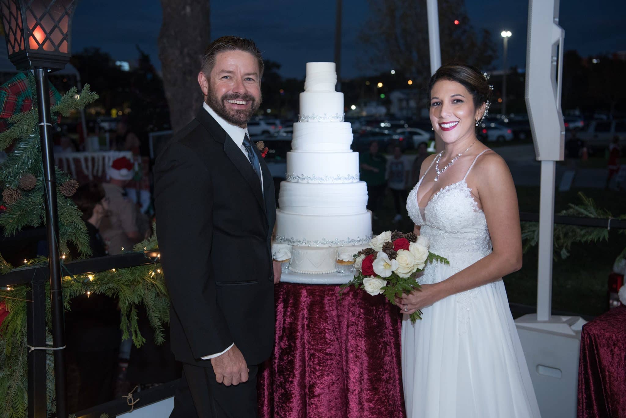 Couple stands on a parade float in wedding attire next to a 7 tiered wedding cake by Got Desserts Lakeland