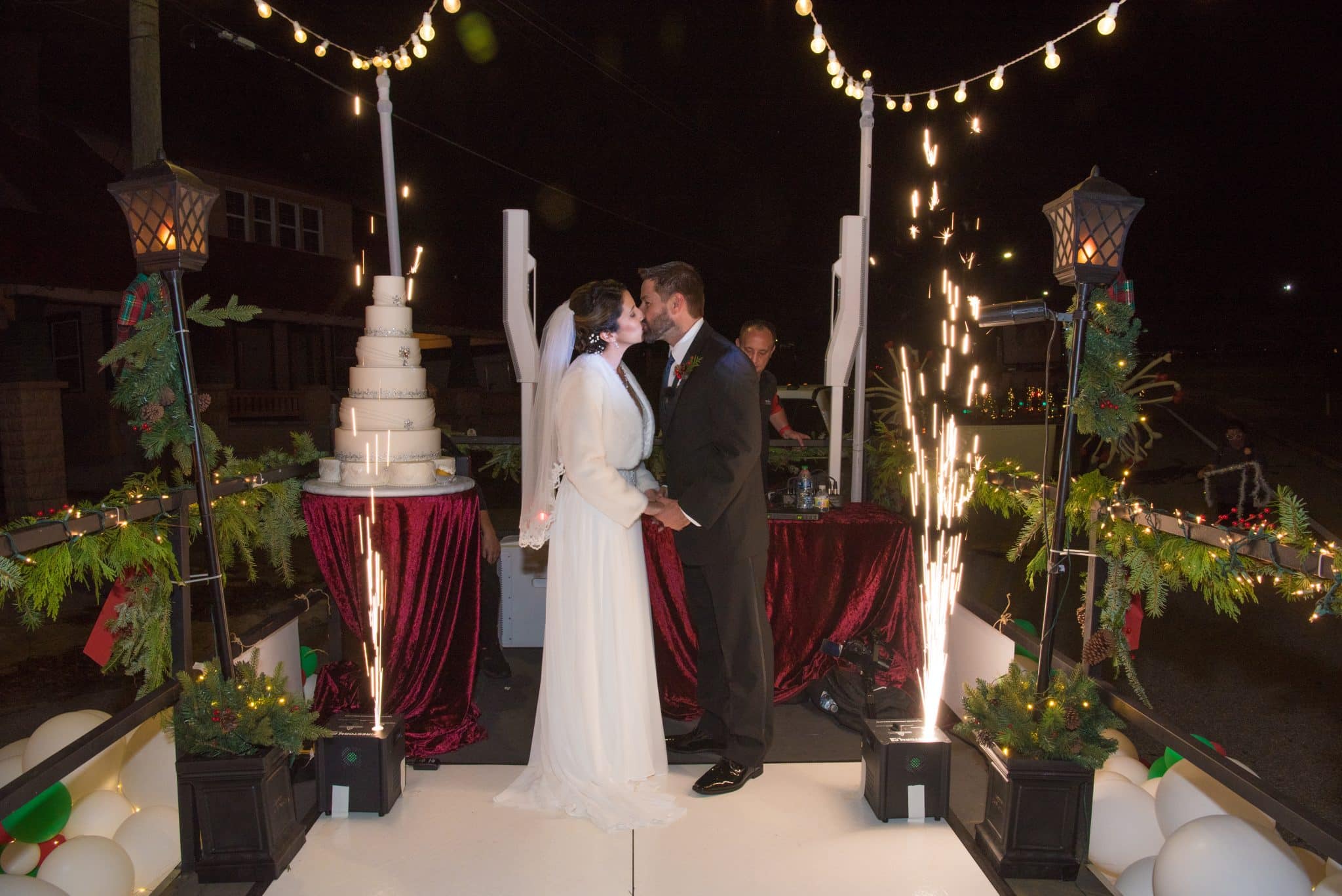 Bride and groom kiss as they stand on a Christmas themed parade float with a white cake and sparks in the background