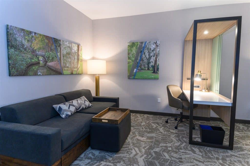 hotel room at hilton garden inn with desk and couch area setup with two paintings hanging on the walls and a floor lamp