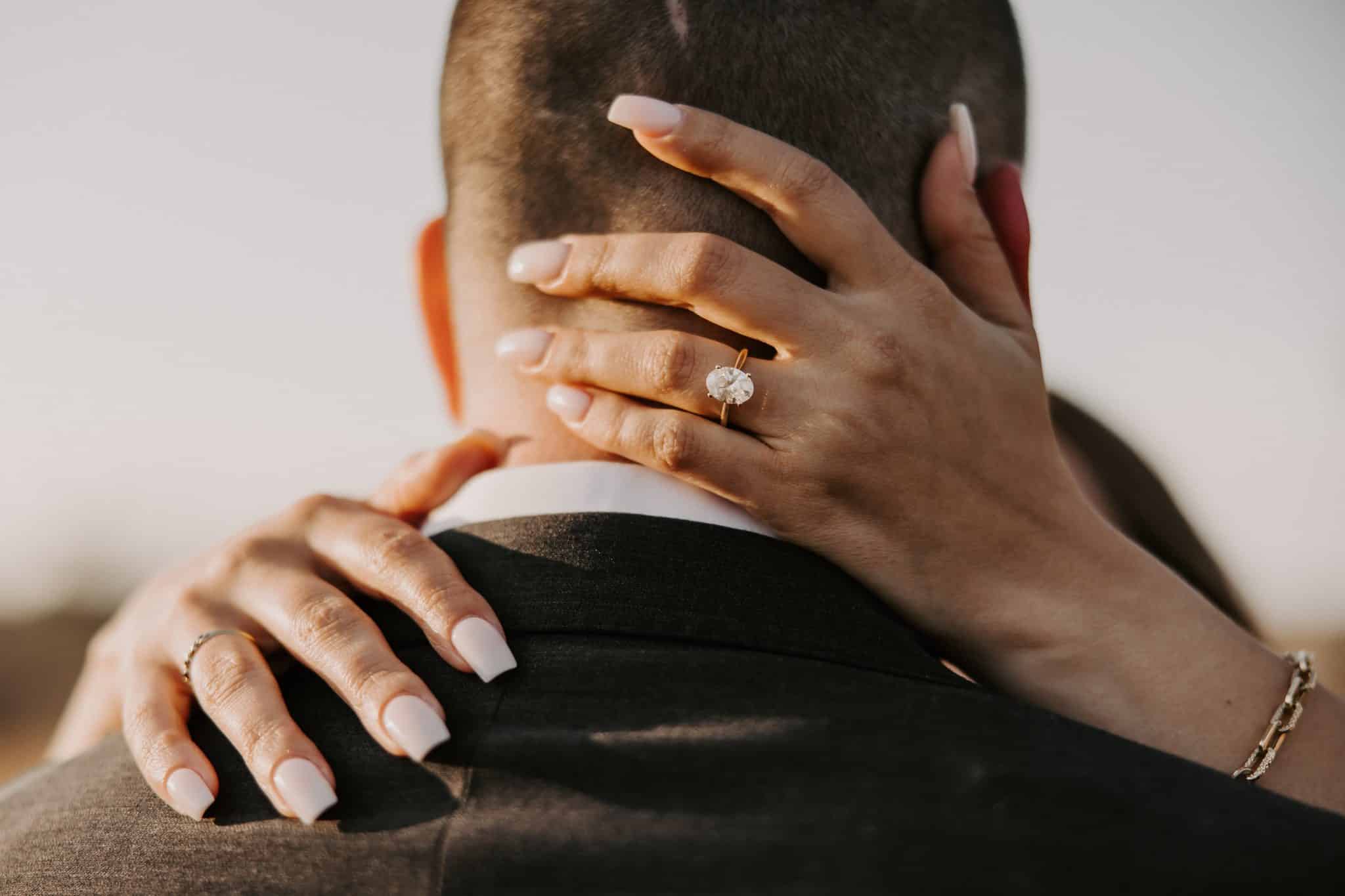 Nicolle wraps her hands around Christian's neck showing her engagement ring, a gold band with a single large oval diamond.