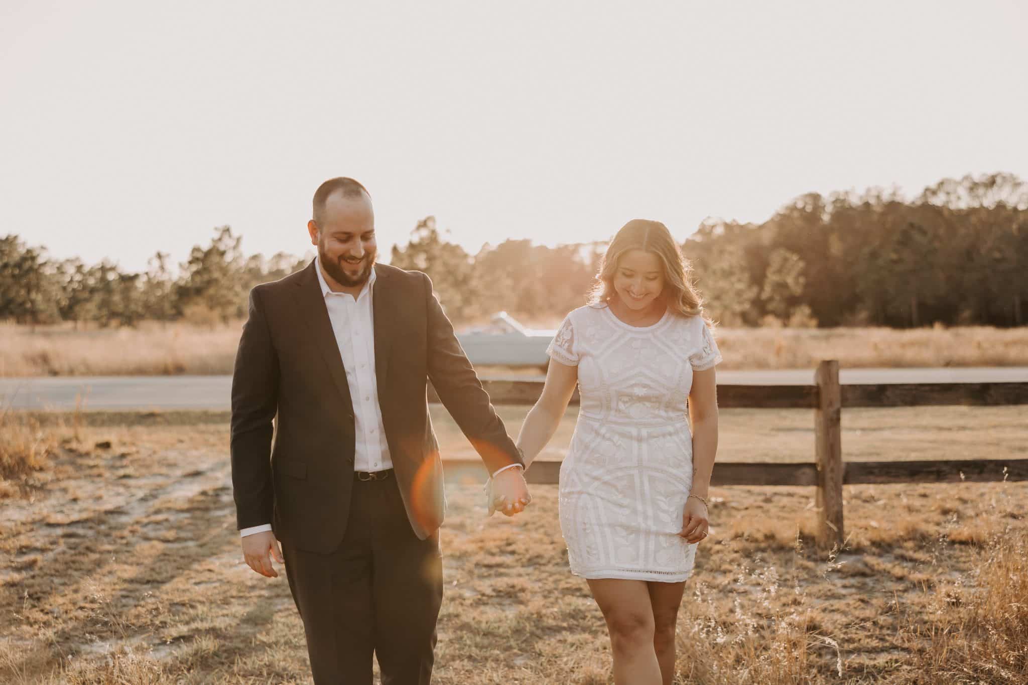 Couple walks hand in hand through a field smiling