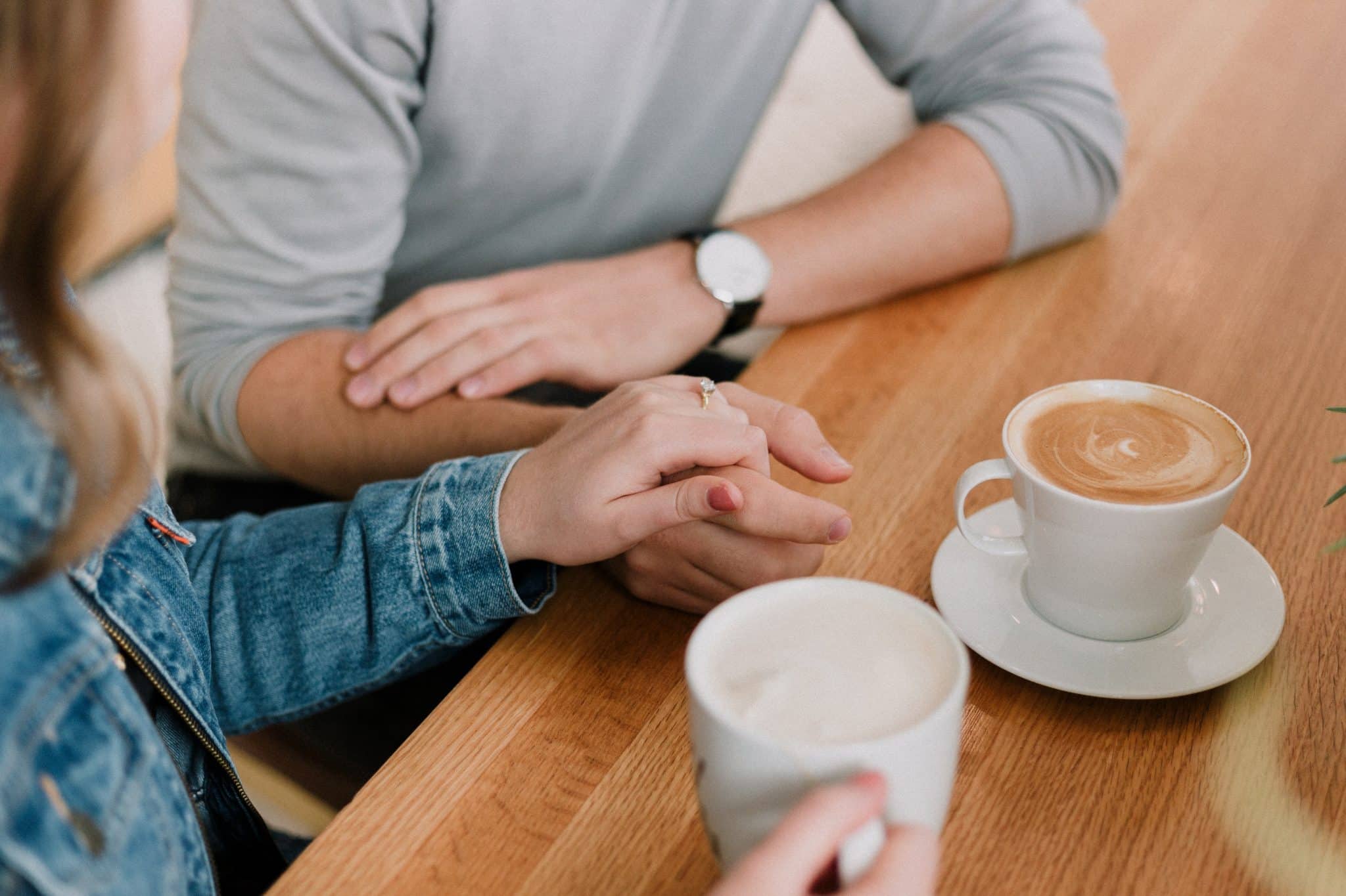Couple holds hands at premarital counseling session while sipping coffee