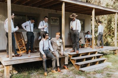Groomsmen in suspenders and dress pants gathering on a rustic wooden porch before a wedding ceremony at Sugar Grove Estate in Lakeland, Florida