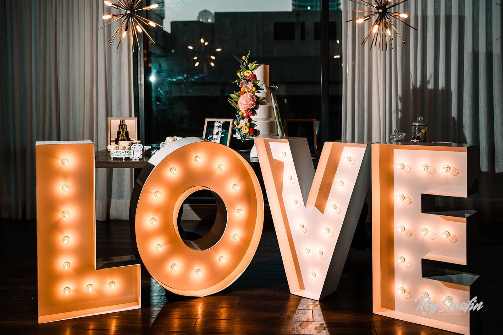 marquee letters spelling love lit up in front of table with wedding cake displayed