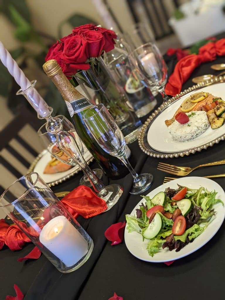 salad and entree set at table with champagne flutes, silver candles and red roses from Latin Raices Catering
