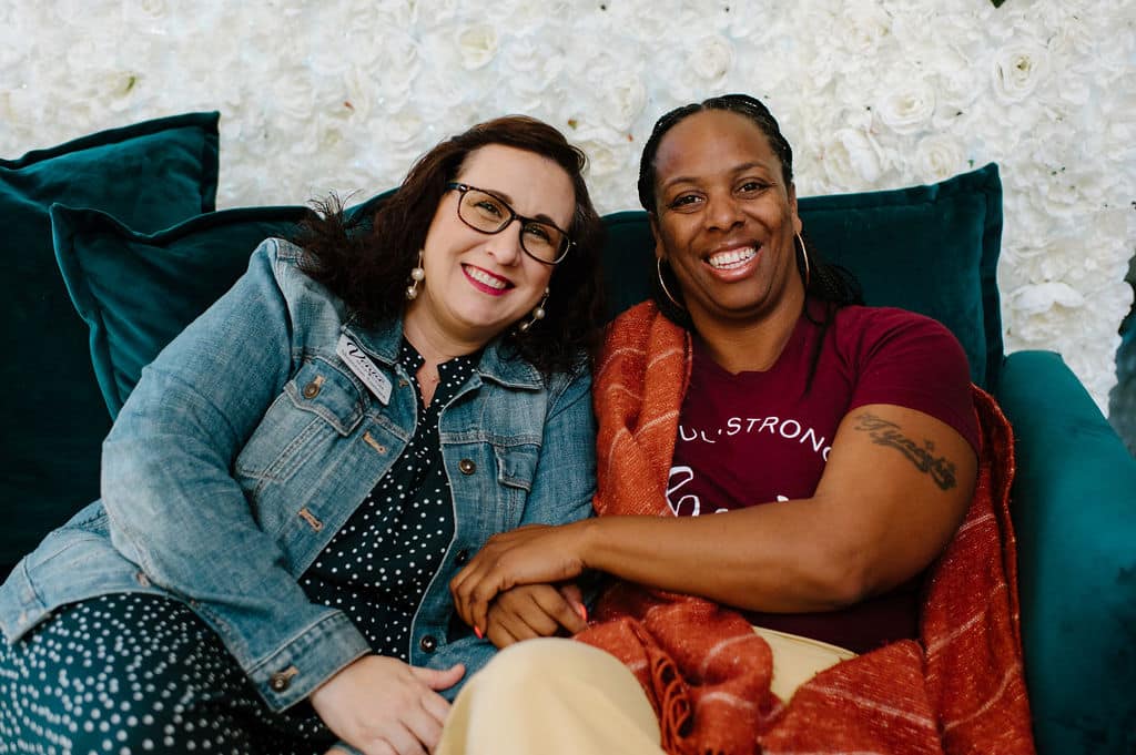 two women sitting on emerald green velvet couch close to each other smiling at the camera for a picture