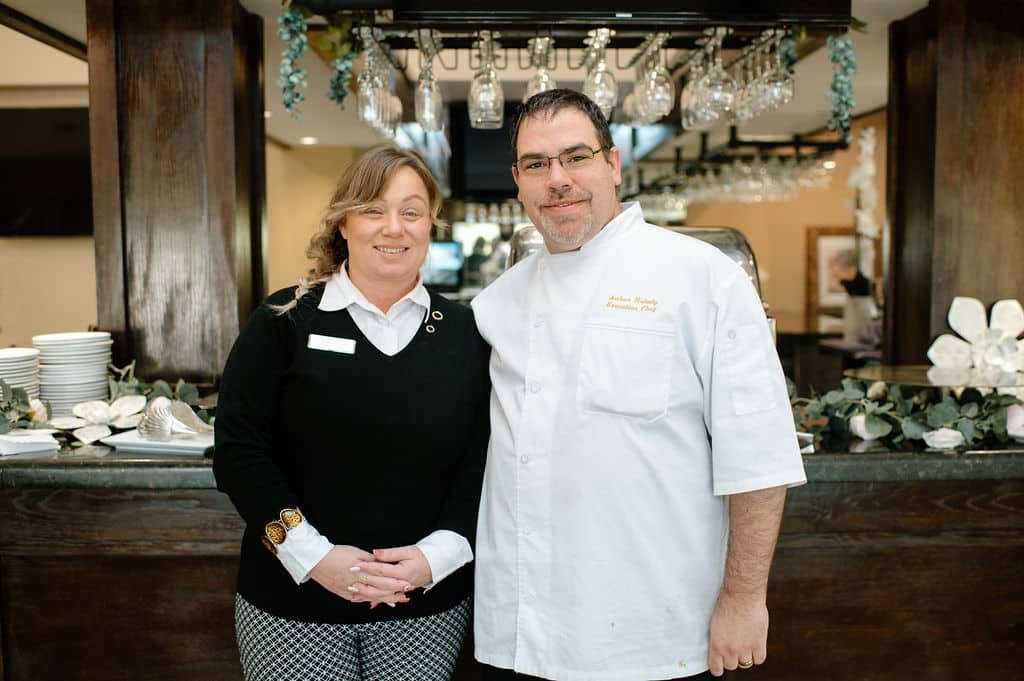 woman standing next to man with chefs coat on in front of wooden bar