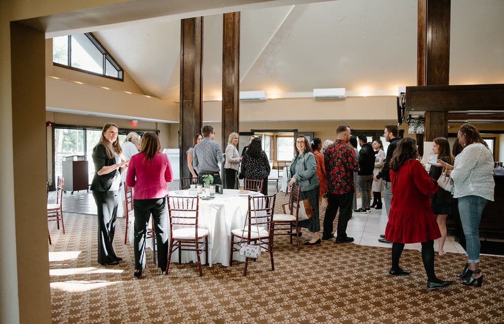 event space setup with tables and chairs as guests stand around chatting with each other while drinking coffee