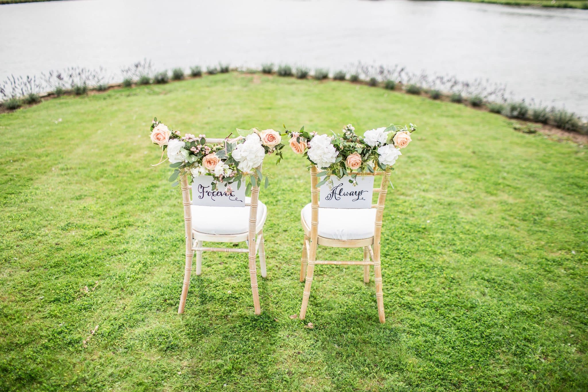 Bride and groom chairs decorated with pink and white flowers and signs reading "forever and always"