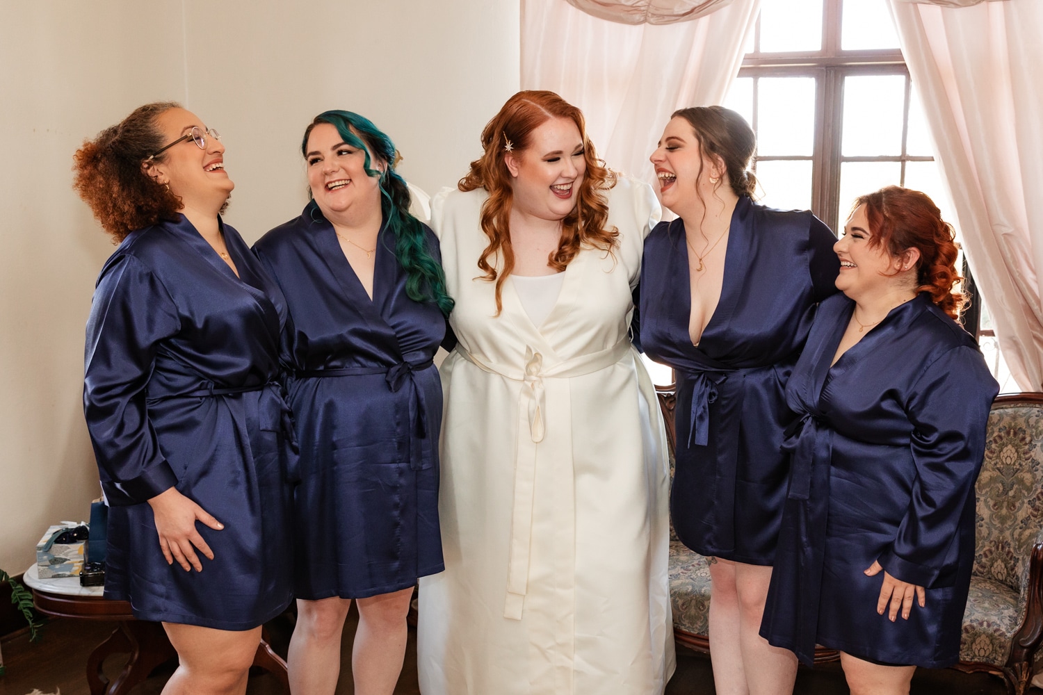 Bride stands with her bridesmaids wearing deep blue silk robes at celestial wedding at howey mansion.