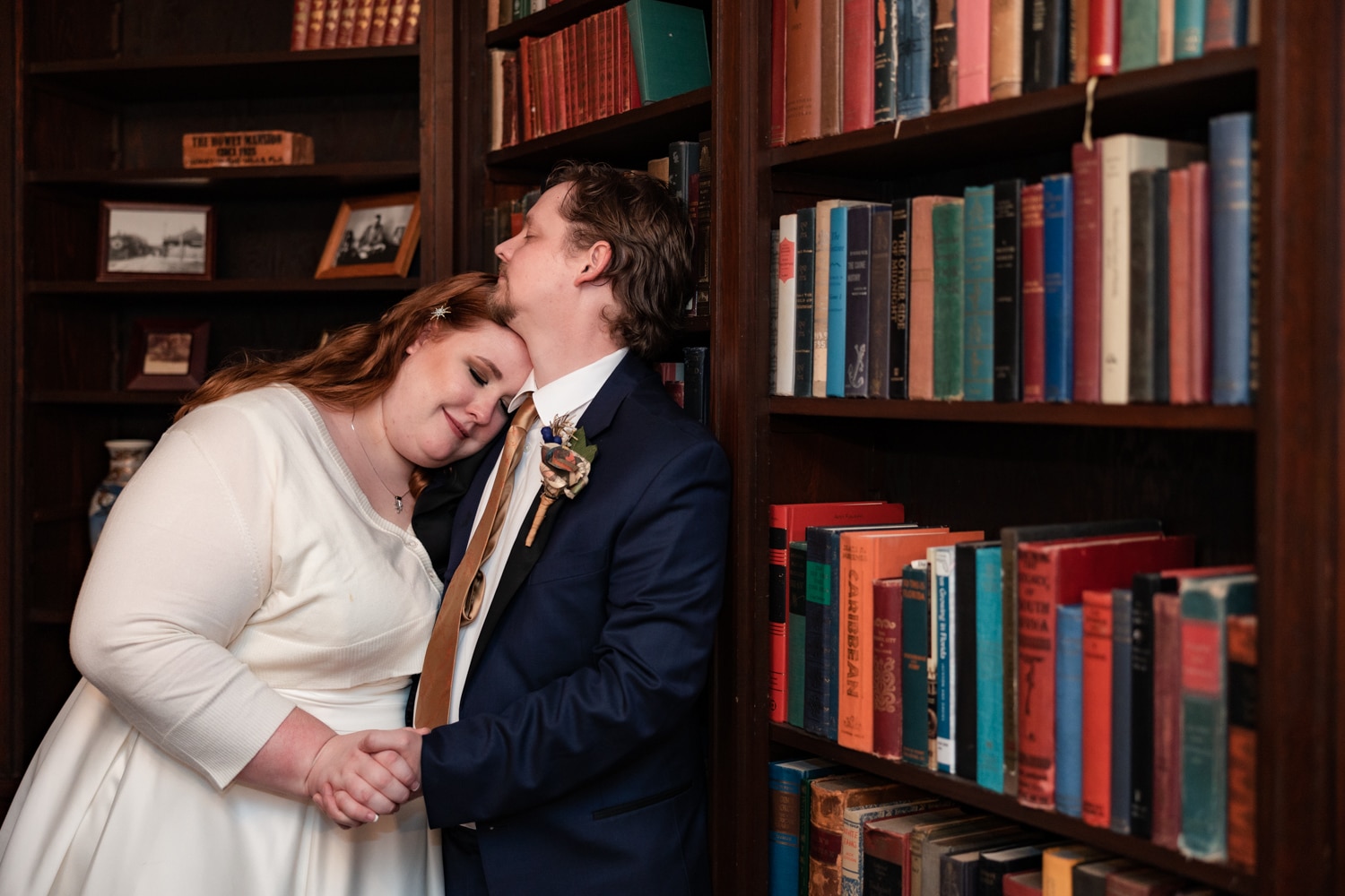 Newlyweds embrace against vintage bookshelf at The Howey Mansion wedding venue in Central Florida