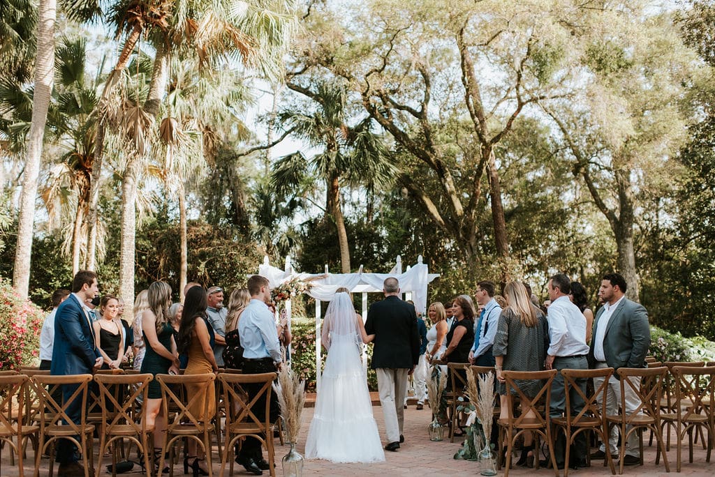 bride and her father walking down the aisle under pines and palms at The Garden Villa