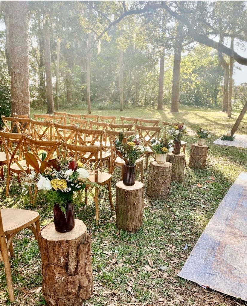rustic outdoor wedding ceremony with log aisle floral arrangements in the woods at The Garden Villa