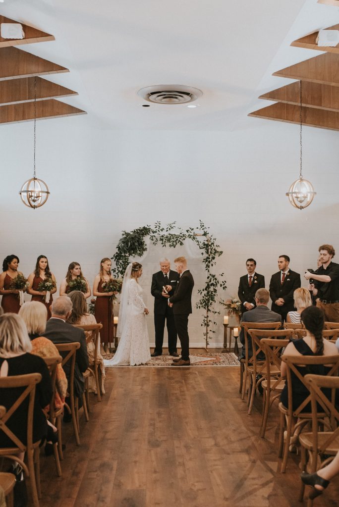 bride and groom at indoor ceremony under wooden beams and floral arch at The Garden Villa