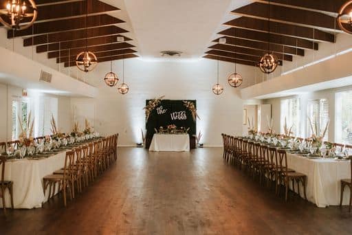 reception room with wooden floors and wooden beams set with long tables and a sweetheart table at the end at The Garden Villa