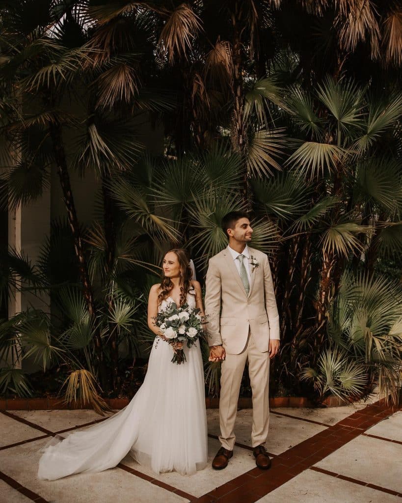 bride and groom in a tan suit agains wall of palm trees at The Garden Villa