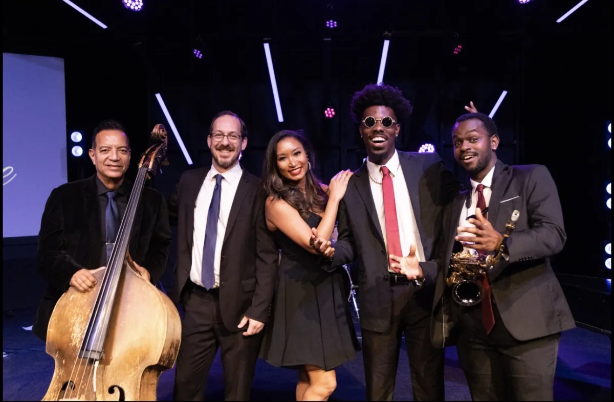 Deanna holding a microphone alongside The Velvet Vibe musicians on stage, with an upright bass and saxophone visible.
