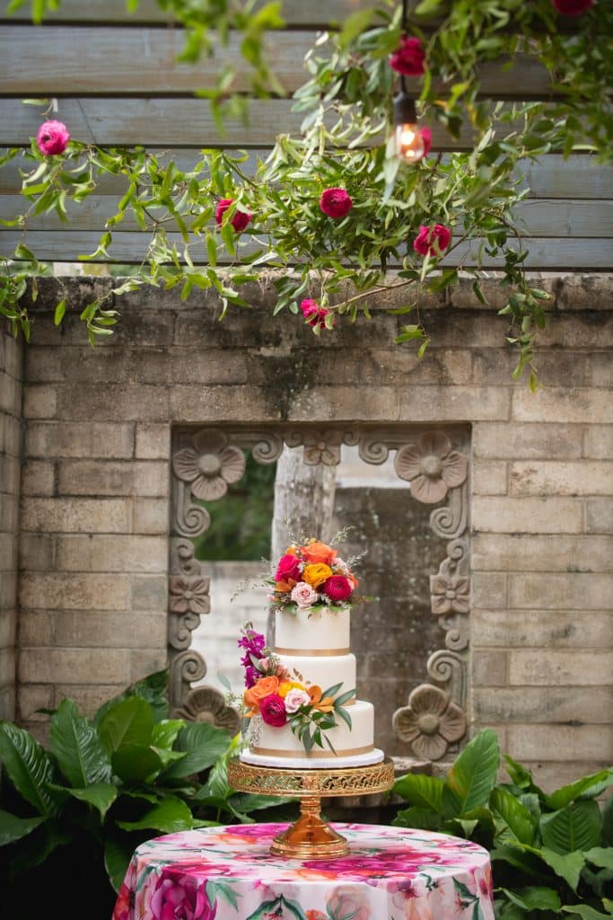 wedding cake decorated with flowers from Dream Design Florist in outdoor courtyard near stone building