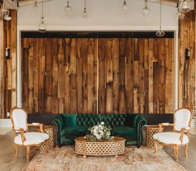 Emerald green tufted velvet Chesterfield sofa with gold ornate accent chairs and a lattice coffee table styled against a rustic reclaimed wood feature wall at St. Johns Golf and Country Club in St. Augustine Florida