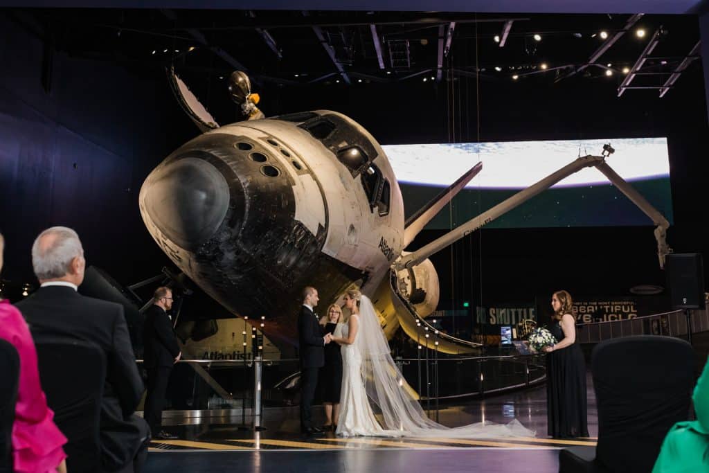bride and groom under old airplane at a museum photographed by Ashley Jane Photography
