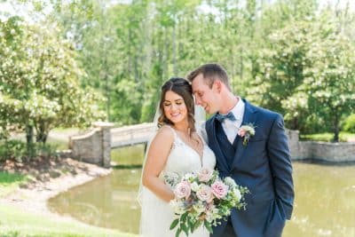Bride and groom share a romantic moment outdoors at St. Johns Golf and Country Club in St. Augustine Florida, with the bride holding a lush pink and white floral bouquet near a scenic waterfront backdrop