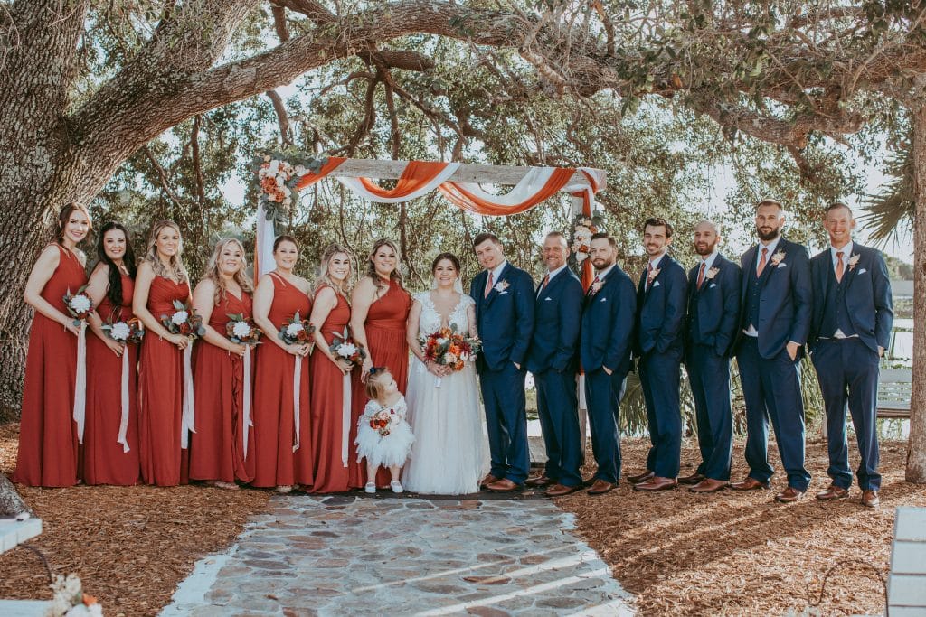 bridal party photo under oak trees with red and white accents in the trees at the Rocking L Ranch Wedding Barn