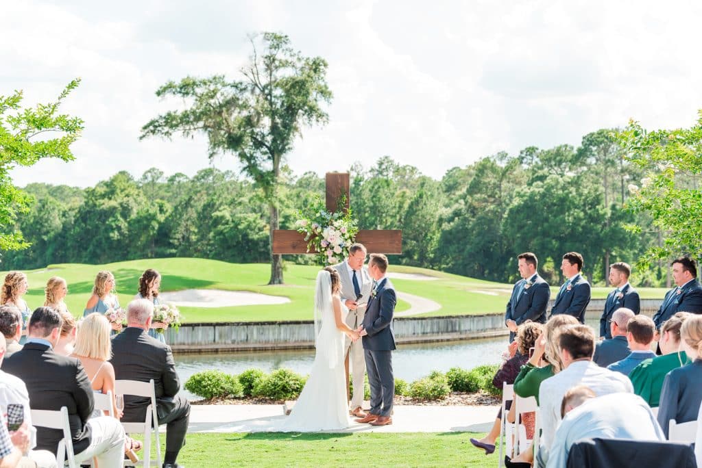 bride and groom saying vows in front of wooden cross with golf course in the background at St. Johns Golf & Country Club