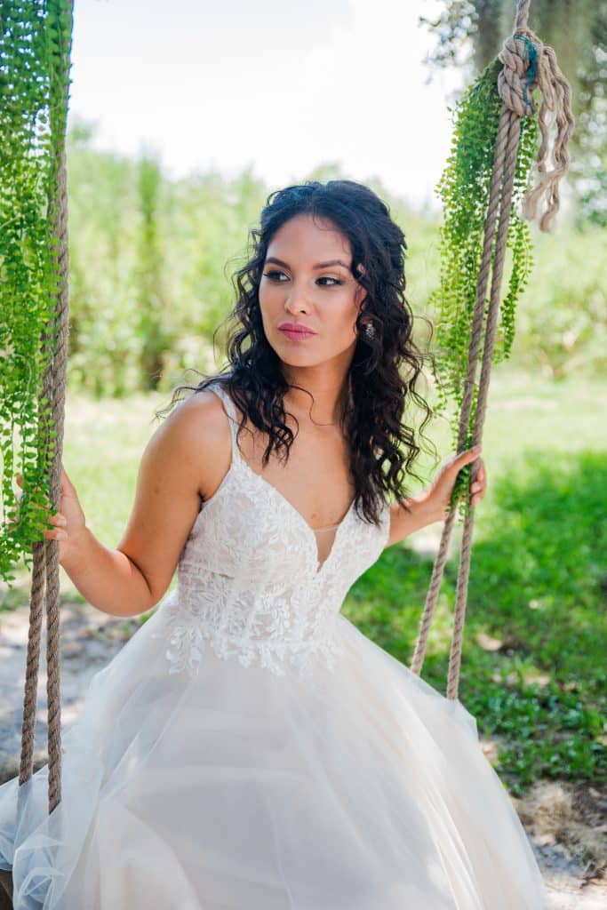 bride sitting on a swing with her hair done in curls by Marci Knuth Hair And Makeup LLC