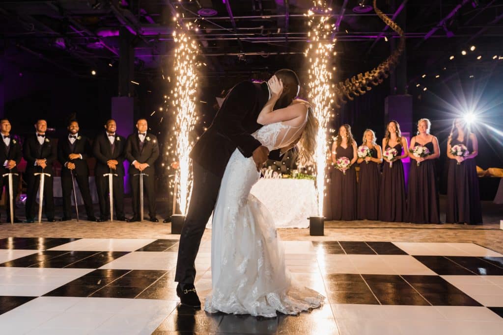 groom dipping bride on black and white dance floor as fireworks go off photographed by Ashley Jane Photography