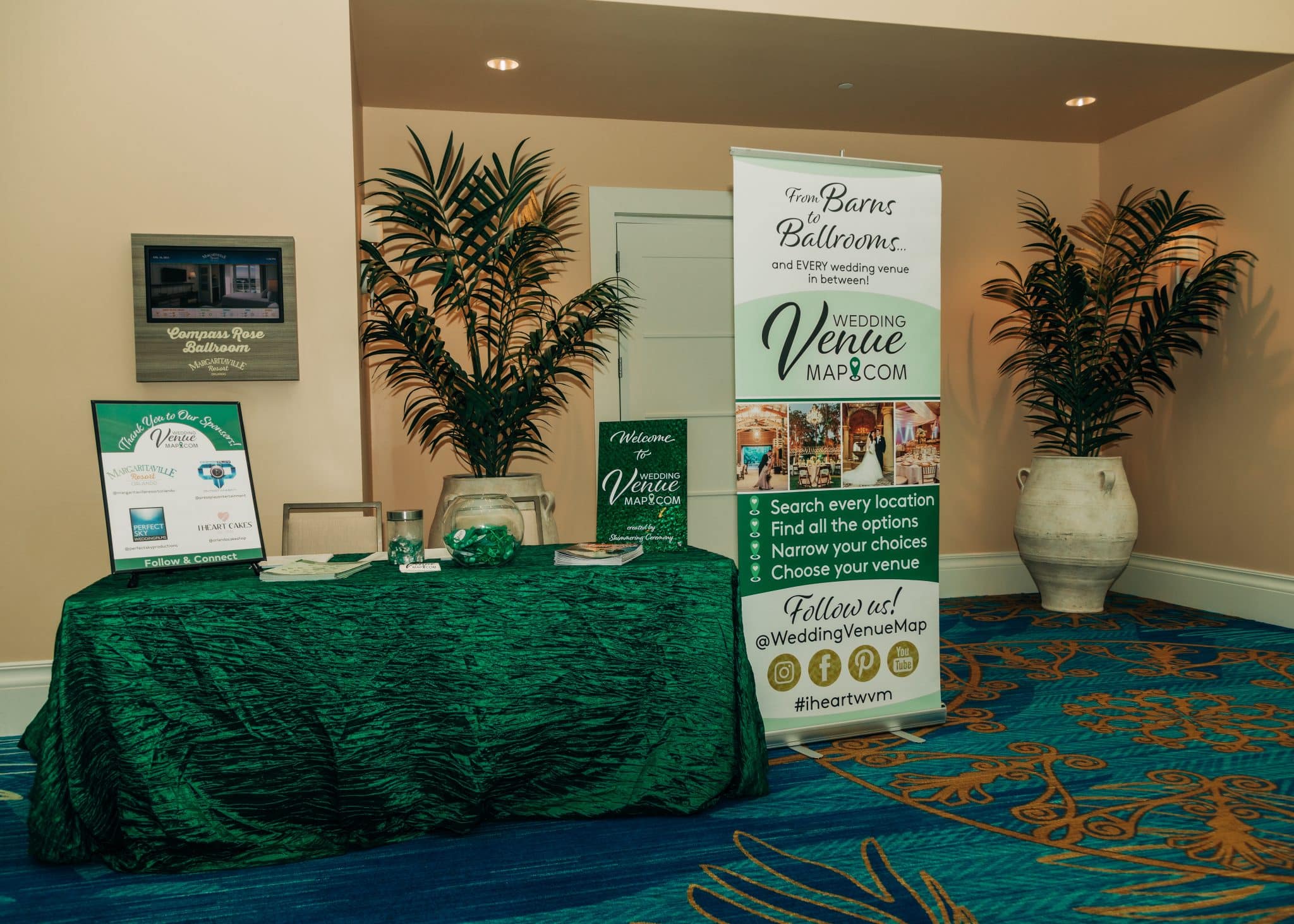 table setup with kelly green linen and advertising signs on top and a company pop up banner next to it in front of doorway with plants on either side