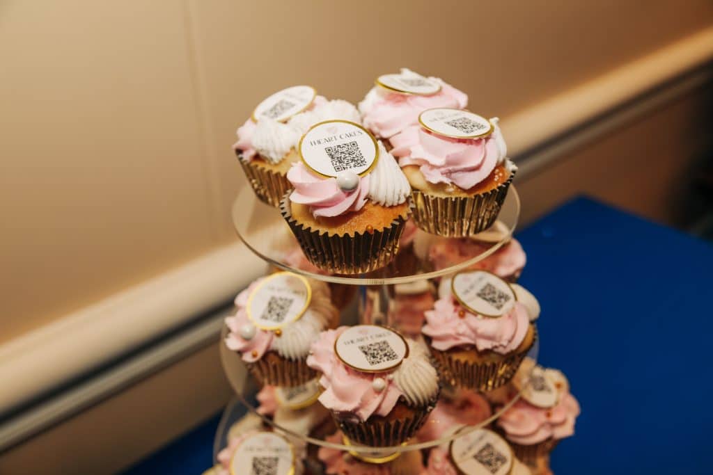 close up image of pink and white iced cupcakes with small circle decoration with QR code on it