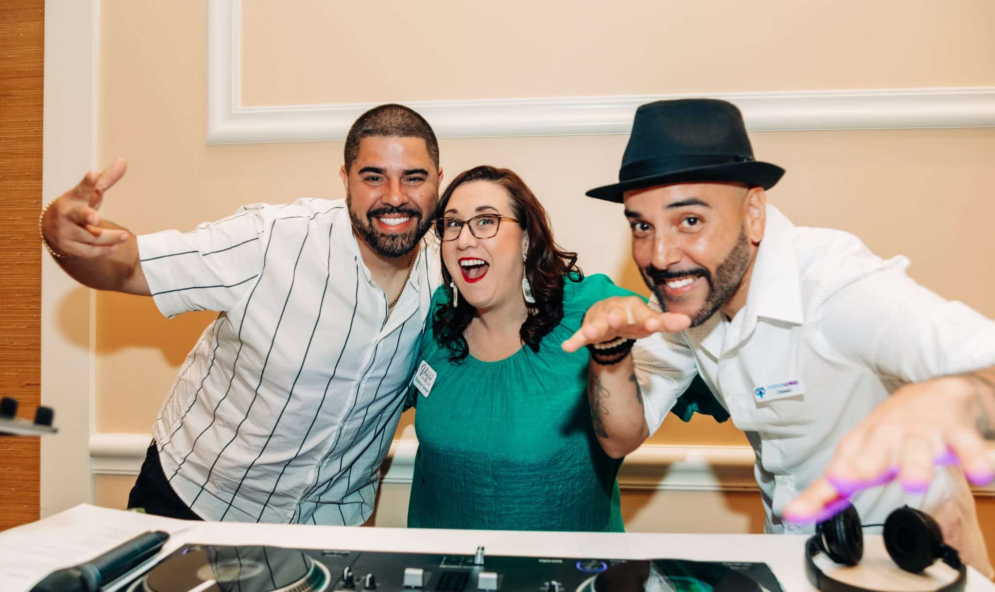 woman stands in between two djs as they stand being the dj mix table posing for a fun picture