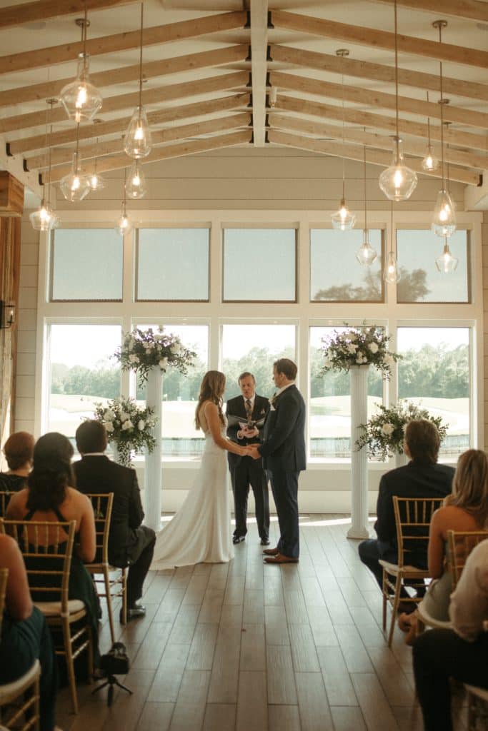 bride and groom say vows against wall of windows at St. Johns Golf & Country Club