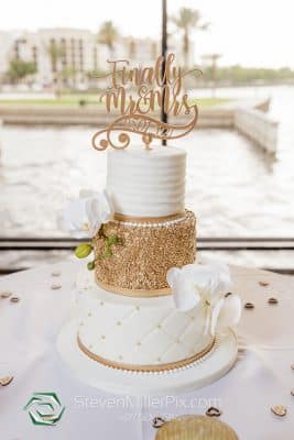Three-tier white and gold wedding cake with quilted fondant, gold sequin middle tier, white orchid accents, and a 'Finally Mr and Mrs' gold cake topper at 520 on the Water waterfront event venue in Sanford, Central Florida